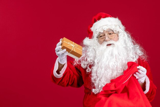 Foto gratuita vista frontal santa claus sosteniendo presente de bolsa llena de regalos para niños en el año nuevo rojo