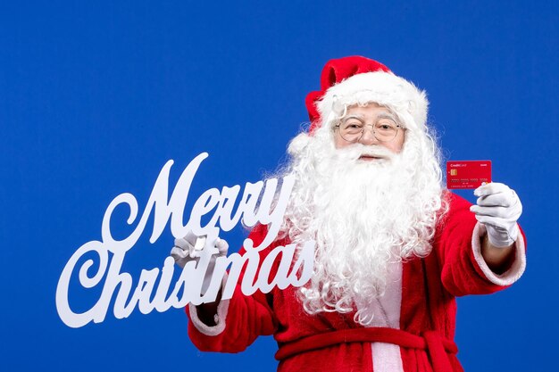 Vista frontal de santa claus con tarjeta bancaria y feliz navidad escribiendo en color azul regalos navideños navidad
