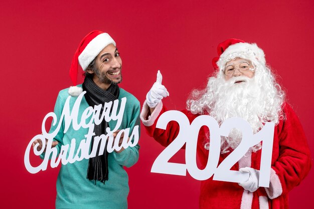 Vista frontal de santa claus con tenencia masculina y escritos de feliz navidad en navidad de año nuevo rojo