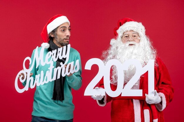 Vista frontal de santa claus con tenencia masculina y escritos de feliz navidad en regalos de navidad rojos