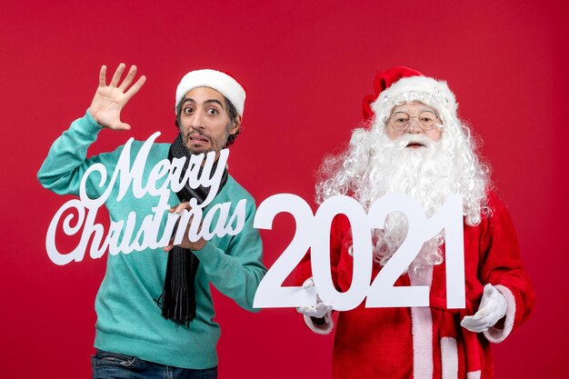 Vista frontal de santa claus con tenencia masculina y escritos de feliz navidad en rojo navidad emoción año nuevo