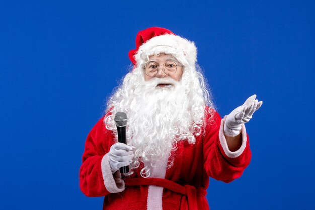 Vista frontal de santa claus con traje rojo y barba blanca sosteniendo el micrófono en la emoción de navidad de vacaciones de año nuevo de color azul