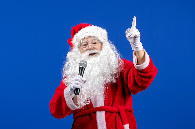 Foto gratuita vista frontal de santa claus con traje rojo y barba blanca sosteniendo el micrófono en el piso azul color año nuevo navidad emoción vacaciones