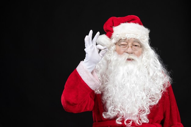 Vista frontal de santa claus en traje rojo clásico con barba blanca en la pared negra