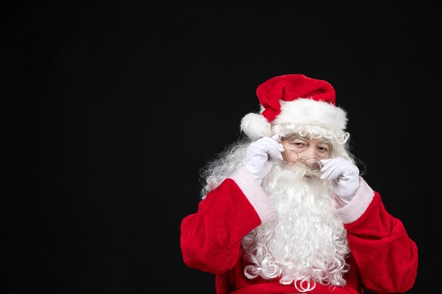 Vista frontal de santa claus en traje rojo clásico con barba blanca de pie sobre la pared negra