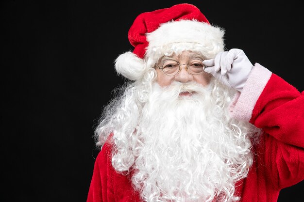 Vista frontal de santa claus en traje rojo clásico con barba blanca de pie sobre la pared negra