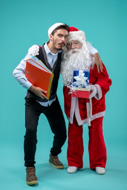 Foto gratuita vista frontal de santa claus con varones jóvenes y presenta en pared azul