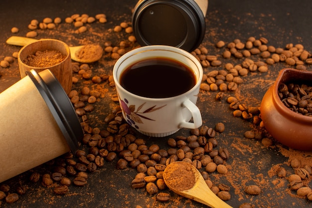 Una vista frontal de las semillas de café marrón con barras de chocolate y una taza de café por toda la superficie oscura y gránulos de granos de semillas de café