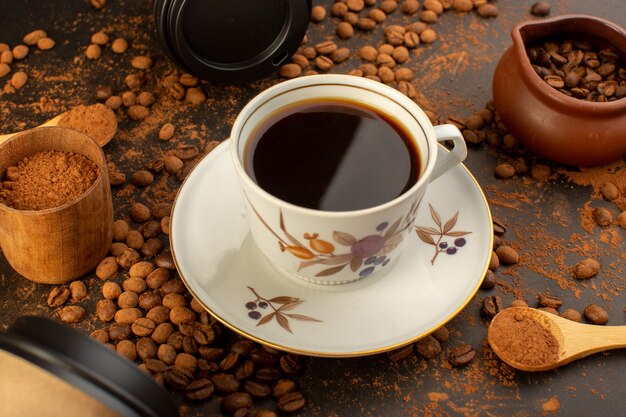 Una vista frontal de semillas de café marrón con barras de chocolate y una taza de café por todo el gránulo de grano de semilla de café de superficie marrón