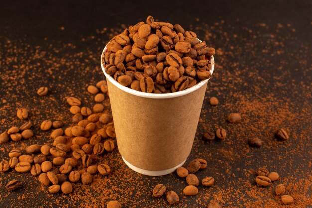 Una vista frontal de las semillas de café marrón dentro de un vaso de plástico sobre la superficie marrón y la semilla de café gránulo de grano oscuro