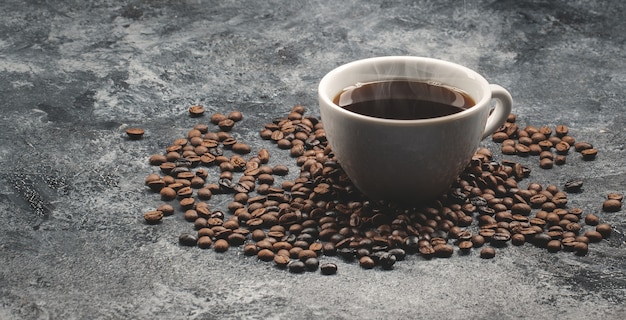 Vista frontal de las semillas de café marrón con una taza de café sobre una superficie oscura