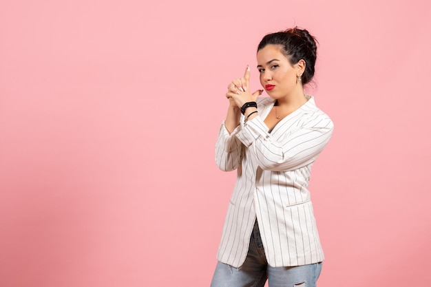 Vista frontal señorita con chaqueta blanca en arma sosteniendo pose sobre fondo rosa dama emociones moda sentimiento color mujer