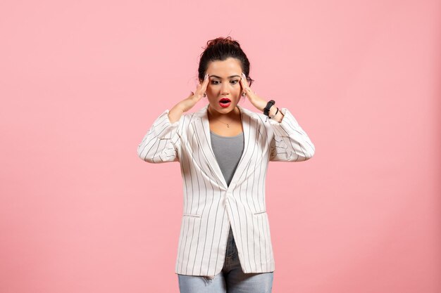 Vista frontal señorita en chaqueta blanca con cara de sorpresa sobre fondo rosa moda mujer emoción color sentimiento dama