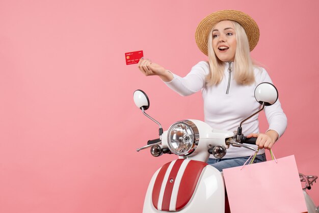 Vista frontal señorita en ciclomotor dando tarjeta sosteniendo bolsas de la compra.