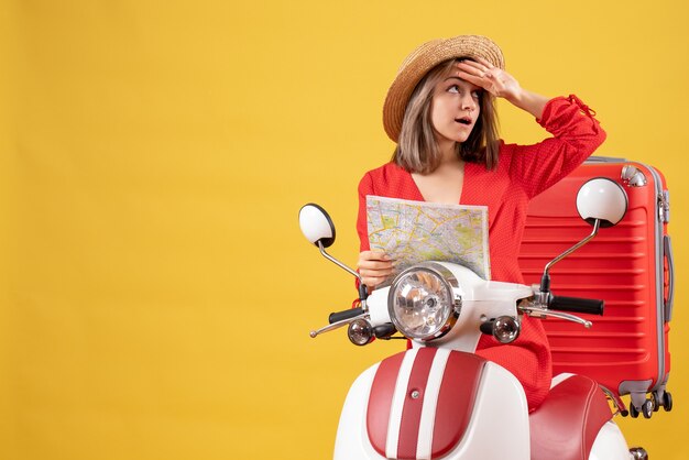 Vista frontal señorita en ciclomotor con maleta roja sosteniendo el mapa poniendo la mano en la frente