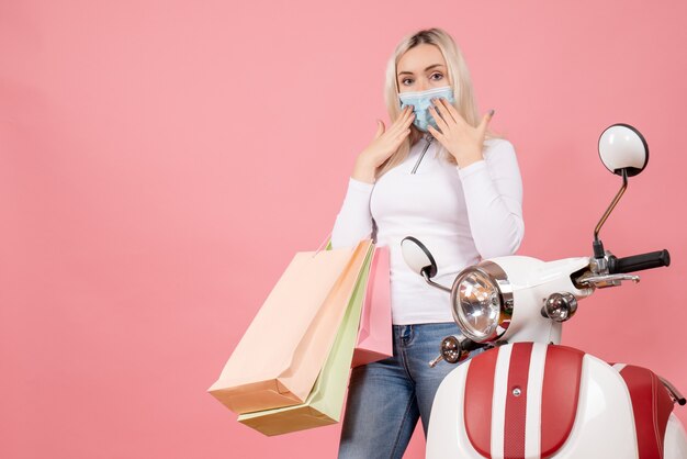 Vista frontal señorita sosteniendo bolsas de la compra poniendo las manos en la cara cerca del ciclomotor