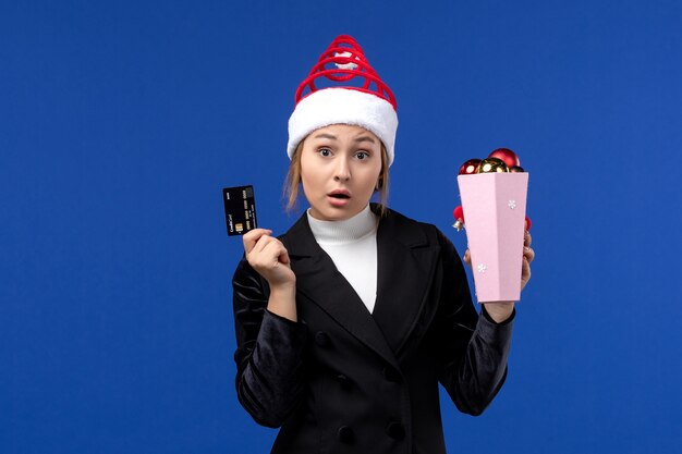 Vista frontal señorita sosteniendo una tarjeta bancaria en la pared azul vacaciones de emoción de año nuevo