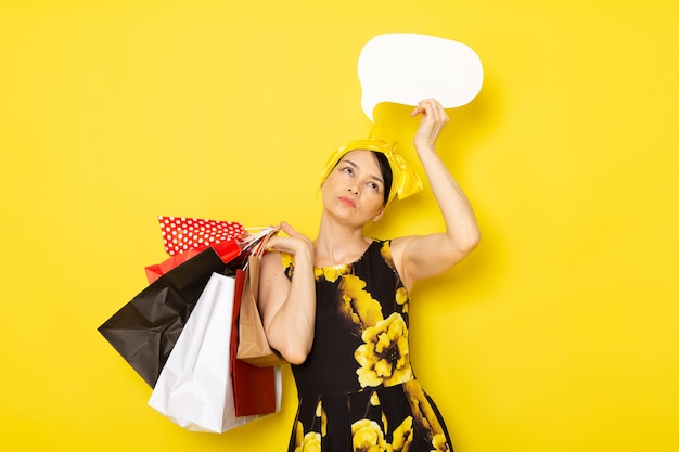 Foto gratuita una vista frontal señorita en vestido de flores amarillo-negro diseñado con vendaje amarillo en la cabeza con paquetes de compras cartel blanco sobre el amarillo