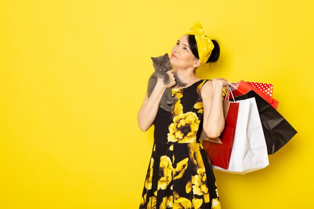 Una vista frontal señorita en vestido de flores amarillo-negro diseñado con vendaje amarillo en la cabeza con paquetes de compras y gatito en el amarillo