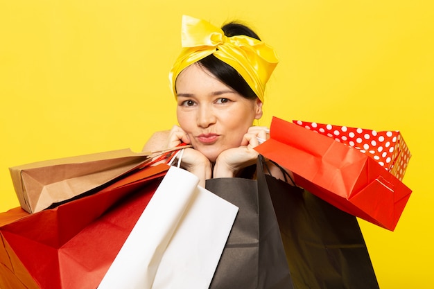 Una vista frontal señorita en vestido de flores amarillo-negro diseñado con vendaje amarillo en la cabeza posando sosteniendo paquetes de compras en el amarillo