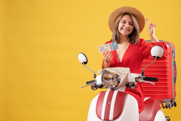 Vista frontal de la señorita en vestido rojo con billete haciendo deseo firmar en ciclomotor