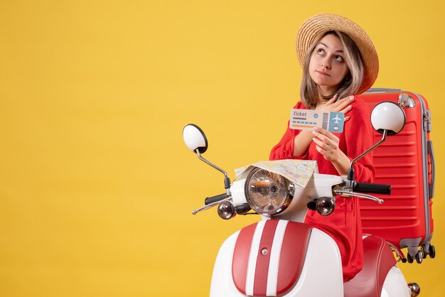 Vista frontal señorita en vestido rojo con boleto mirando hacia arriba en ciclomotor
