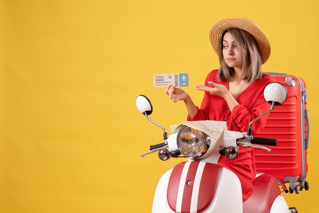 Vista frontal señorita en vestido rojo y sombrero panamá con boleto en ciclomotor