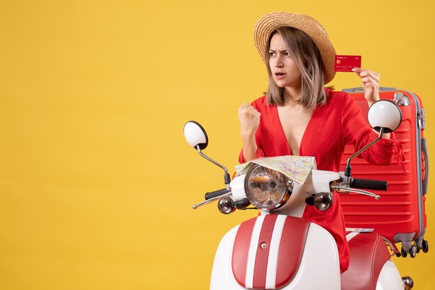 Vista frontal señorita en vestido rojo con tarjeta de crédito cerca de ciclomotor