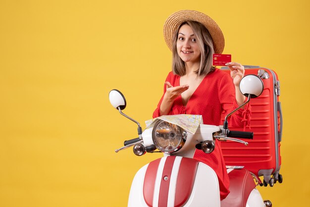 Vista frontal señorita en vestido rojo con tarjeta de descuento en ciclomotor