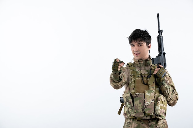 Vista frontal del soldado masculino con ametralladora en pared blanca de camuflaje