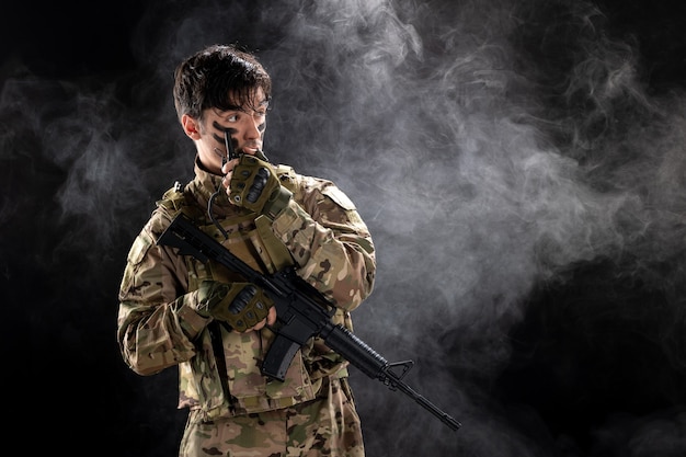 Vista frontal del soldado masculino con ametralladora con walkie-talkie pared negra