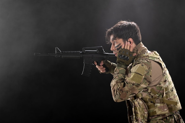 Vista frontal del soldado masculino luchando con rifle en una pared oscura
