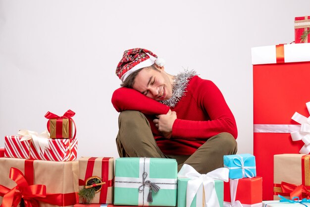 Vista frontal soñador joven con máscara sentado alrededor de regalos de Navidad