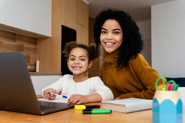 Vista frontal de sonriente adolescente ayudando a hermanita durante la escuela en línea con tableta