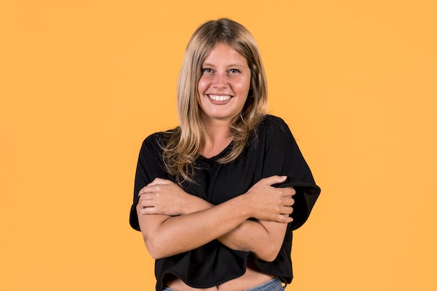 Vista frontal de la sonriente joven abrazando a sí misma en la superficie amarilla