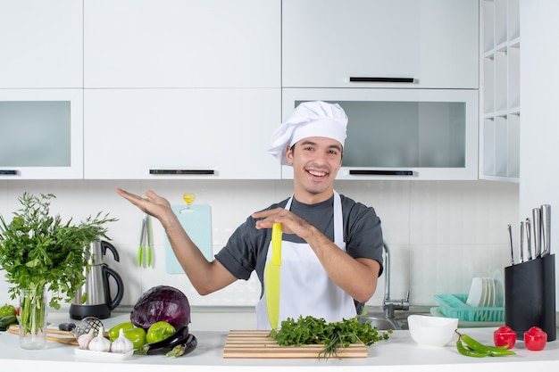 Vista frontal sonriente joven chef en uniforme apuntando a la izquierda