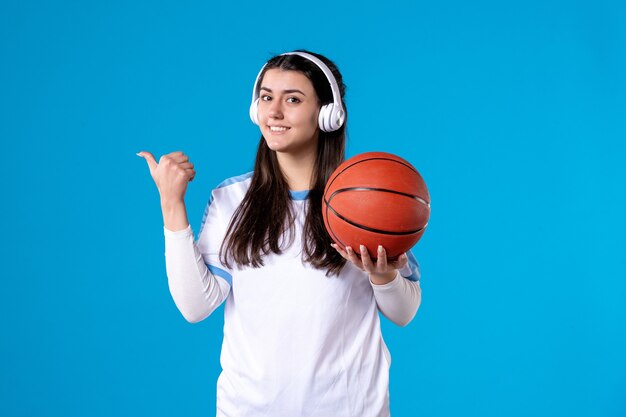 Vista frontal sonriente joven mujer con auriculares sosteniendo baloncesto