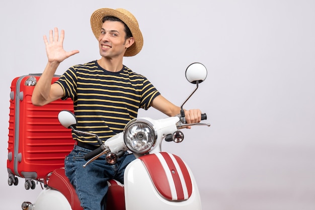 Vista frontal del sonriente joven con sombrero de paja en ciclomotor agitando la mano