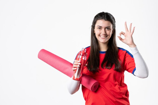 Vista frontal sonriente mujer joven en ropa deportiva con estera de yoga