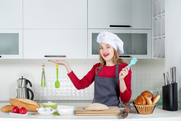 Vista frontal sonriente mujer rubia con sombrero de cocinero y delantal con cepillo en la cocina