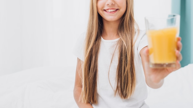 Vista frontal sonriente niña sosteniendo un vaso de jugo de naranja