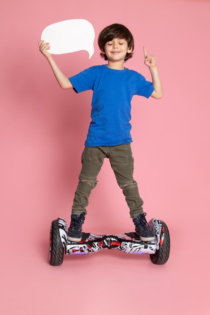 Una vista frontal sonriente niño en camiseta azul y pantalones de color caqui montando segway en el piso rosa