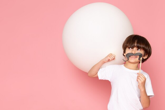 Una vista frontal sonriente niño pequeño en camiseta blanca con bola blanca en el piso rosa