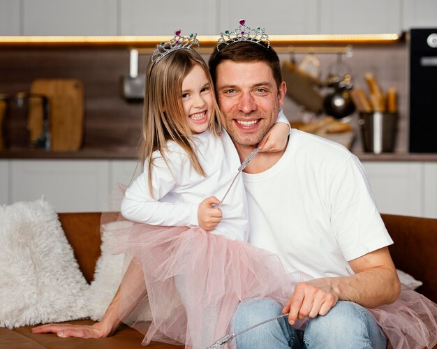 Vista frontal de sonriente padre e hija jugando con tiara y varita juntos