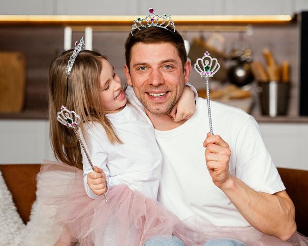 Vista frontal de sonriente padre e hija jugando con tiara y varita