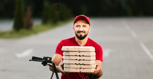 Foto gratuita vista frontal sonriente repartidor sosteniendo cajas de pizza