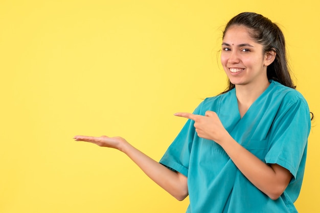 Vista frontal sonrió doctora en uniforme de pie sobre fondo amarillo aislado