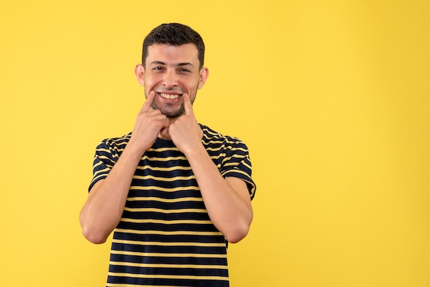 Vista frontal sonrió macho joven en camiseta a rayas blanco y negro fondo amarillo aislado