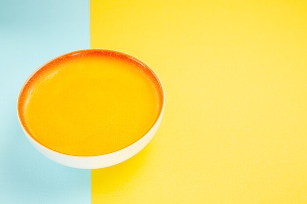 Vista frontal de la sopa de calabaza dentro de la placa en color amarillo-azul plato de sopa de mesa