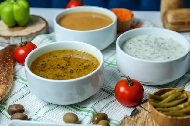 Vista frontal sopa de pollo con lentejas y sopa de yogurt con tomates y aceitunas sobre la mesa